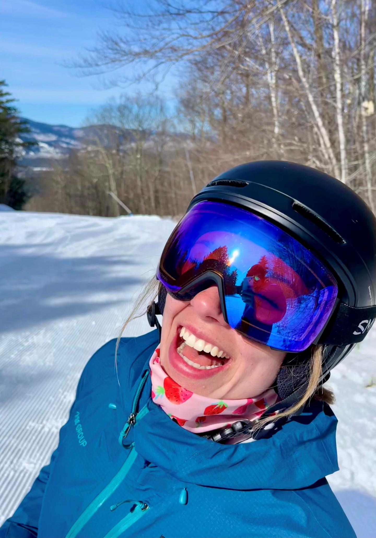 Amelya smiling wearing a ski helmet and goggles on a sunny day