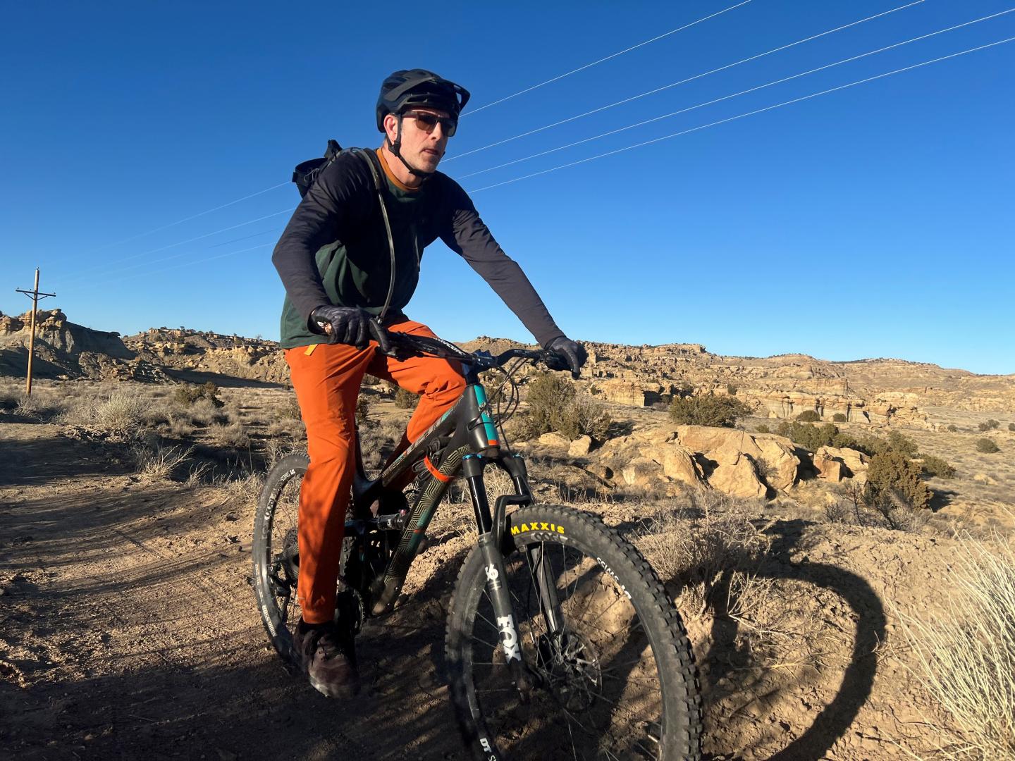 Patrick riding bike in desert wearing orange pants and black jacket with a blue sky